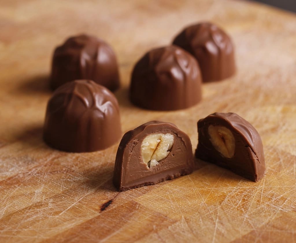 Bombons de chocolate numa tábua de madeira, um deles cortado com recheio de banana