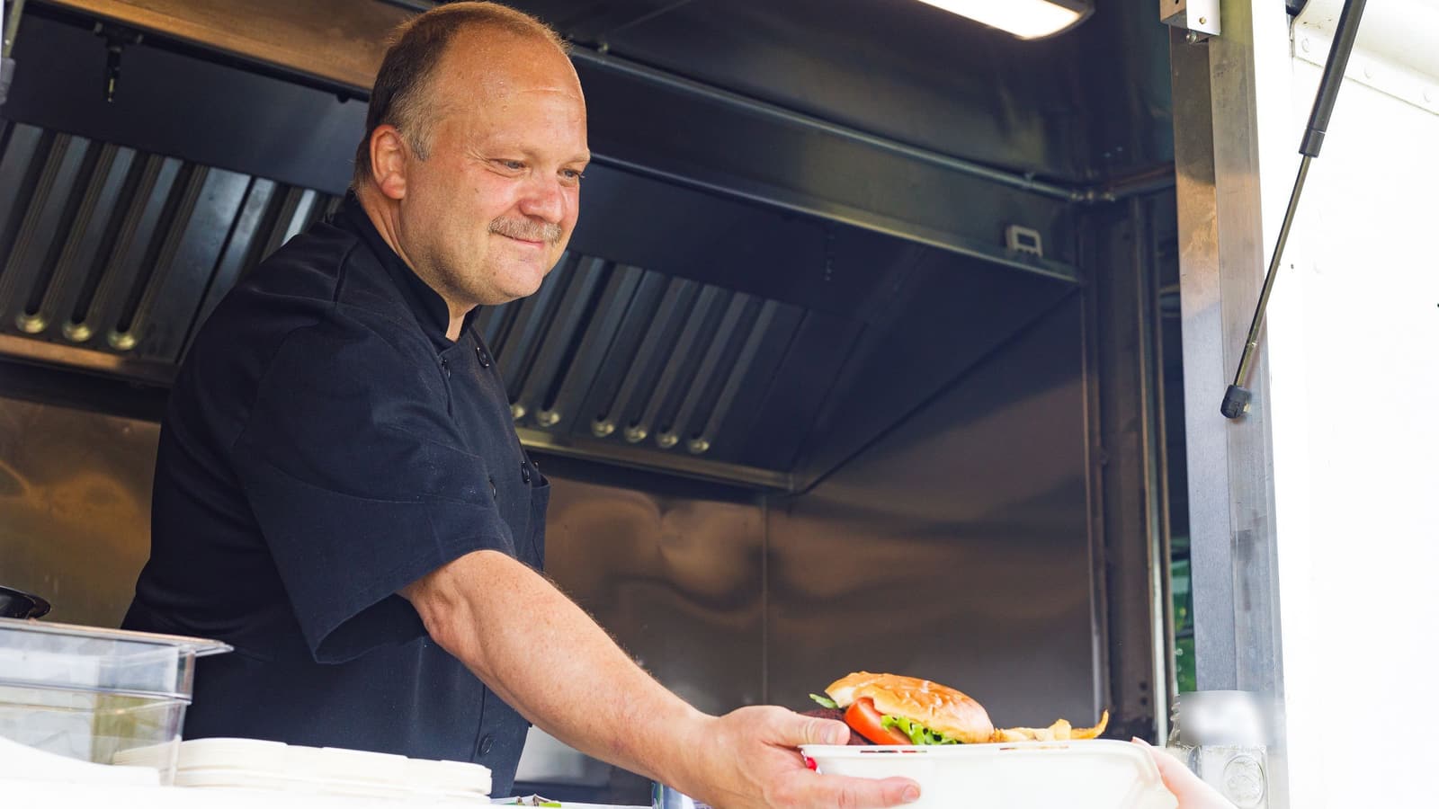 Cozinheiro na janela aberta do trailer entregando um hambúrguer com batata frita a um cliente