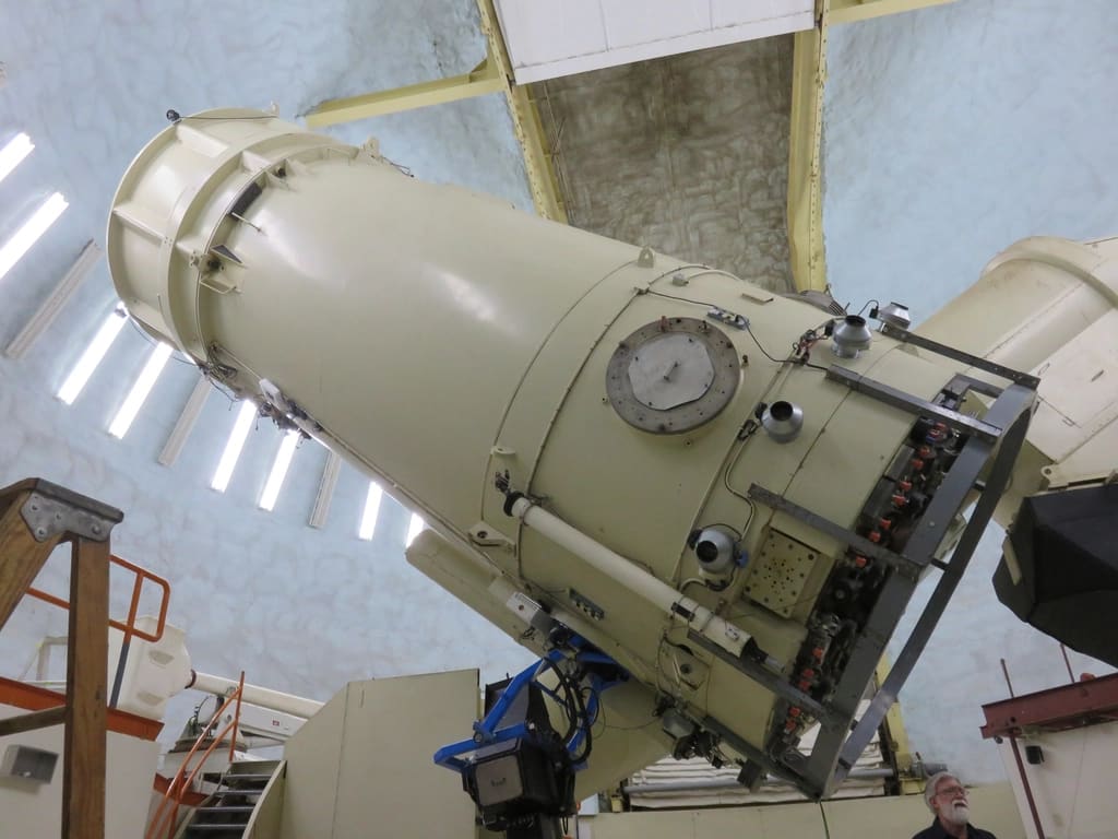 Telescópio grande e antigo, de metal claro, dentro de uma cúpula de observatório