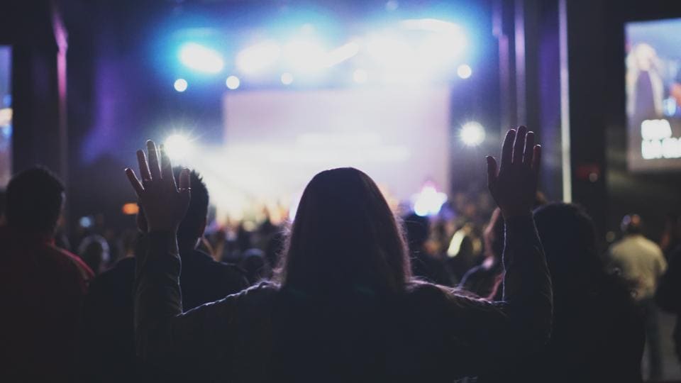 Plateia de costas com os braços levantados diante de um palco iluminado