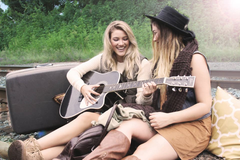 Duas mulheres sentadas na grama, uma tocando violão