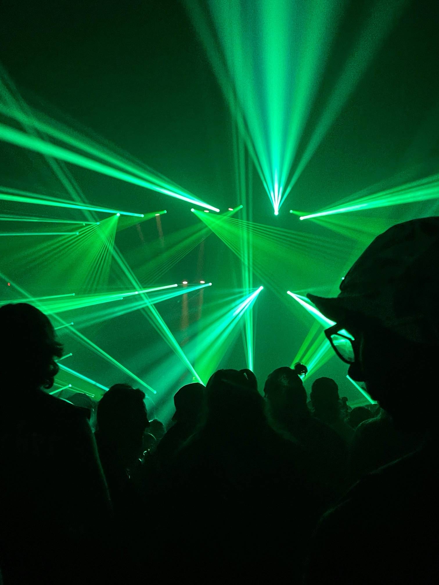 Raios de laser verdes sobre a pista de uma festa, com a plateia em silhueta