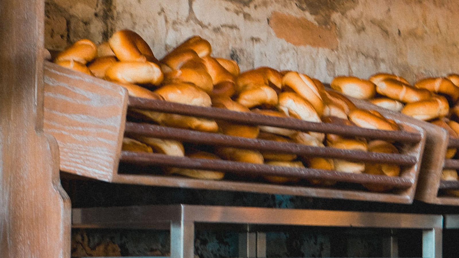Pães frescos em prateleiras de madeira, ao lado das assadeiras