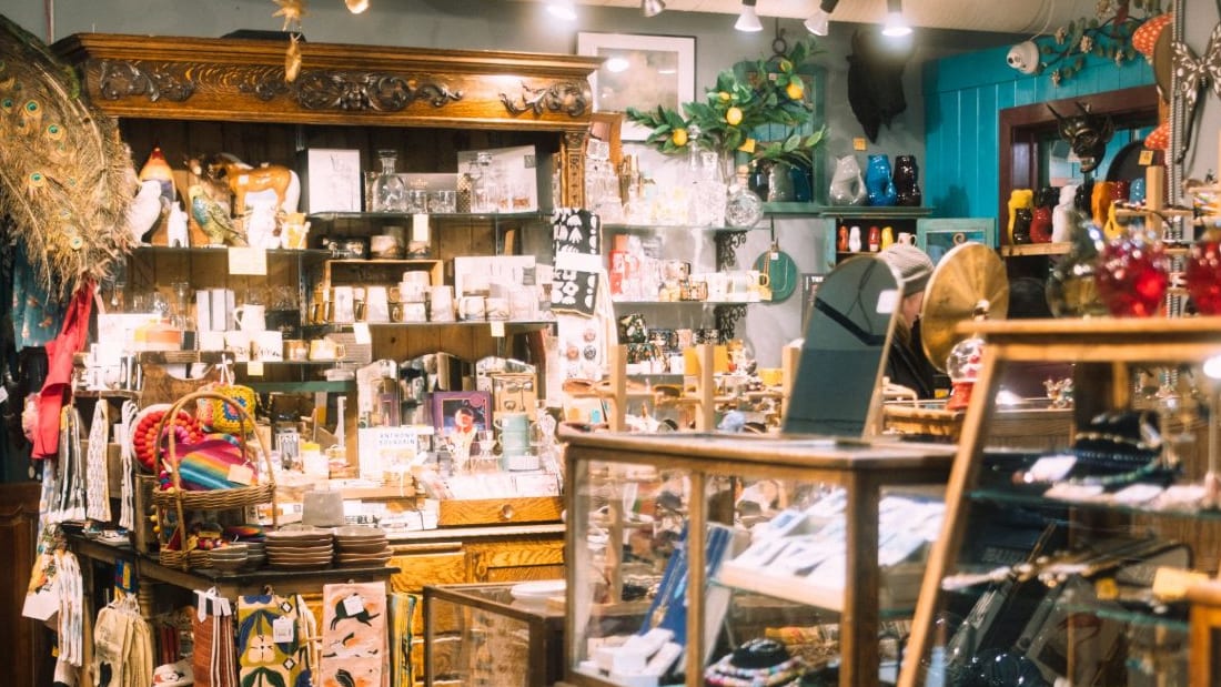 Interior de uma loja de presentes, com móveis de madeira e vitrines cheias de louças, vidros e objetos de decoração
