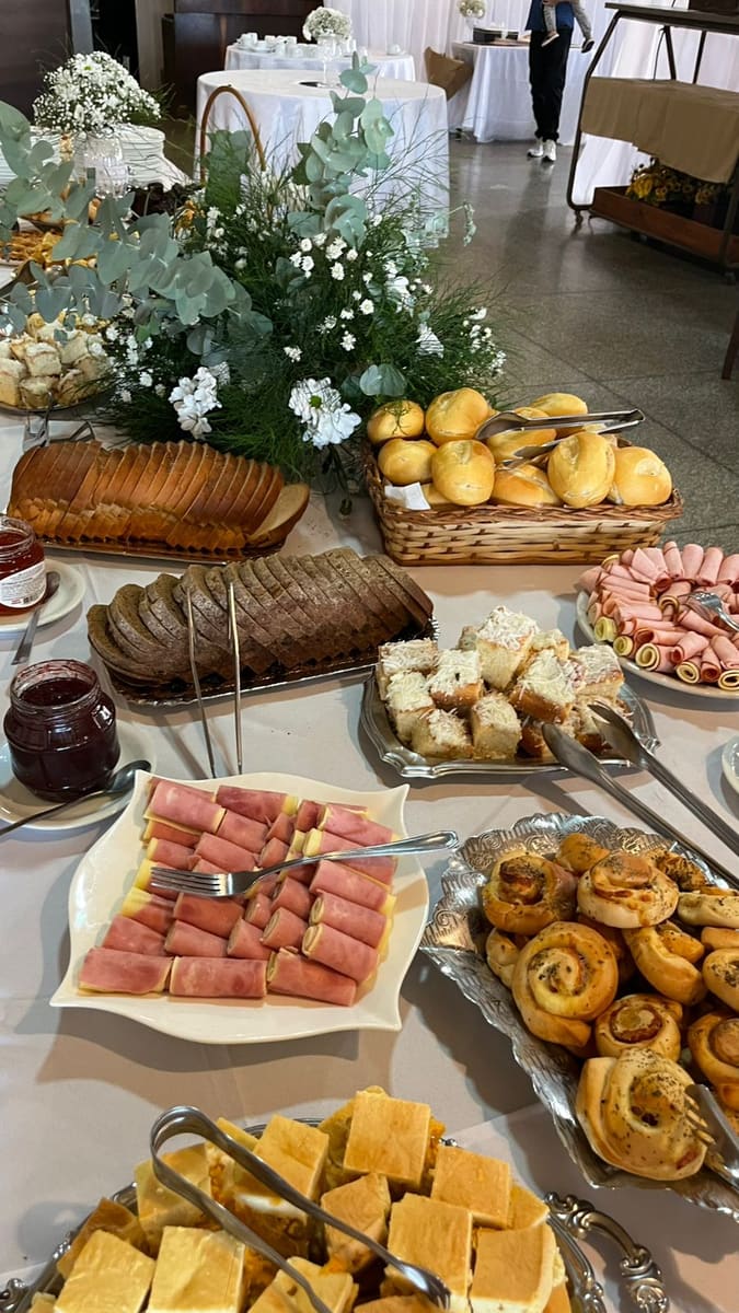 Mesa de festa com pães, frios, salgados e flores brancas