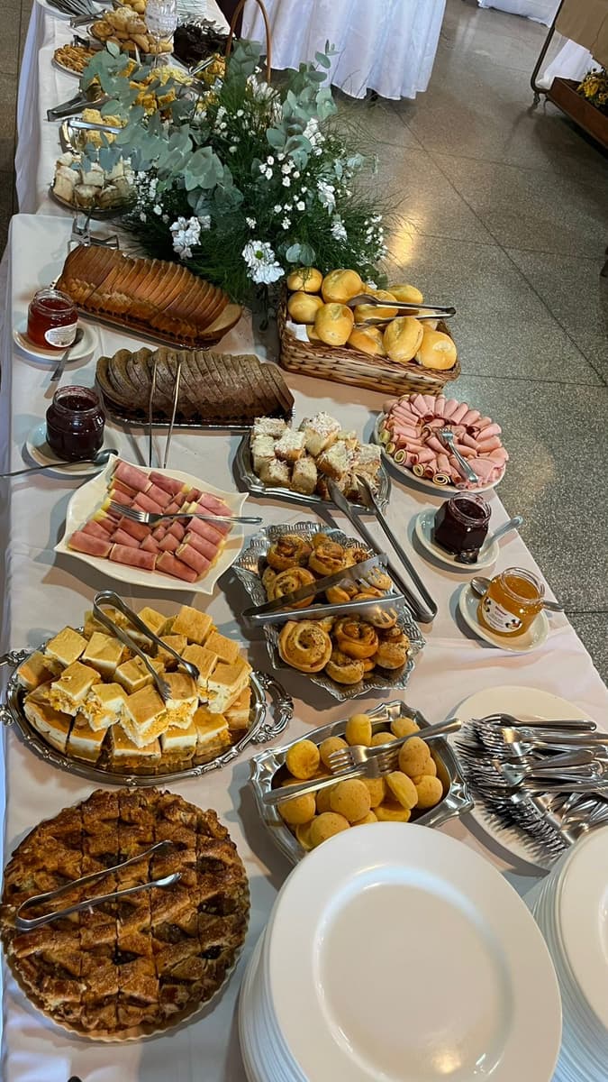 Mesa longa de festa com pães, frios, doces e flores