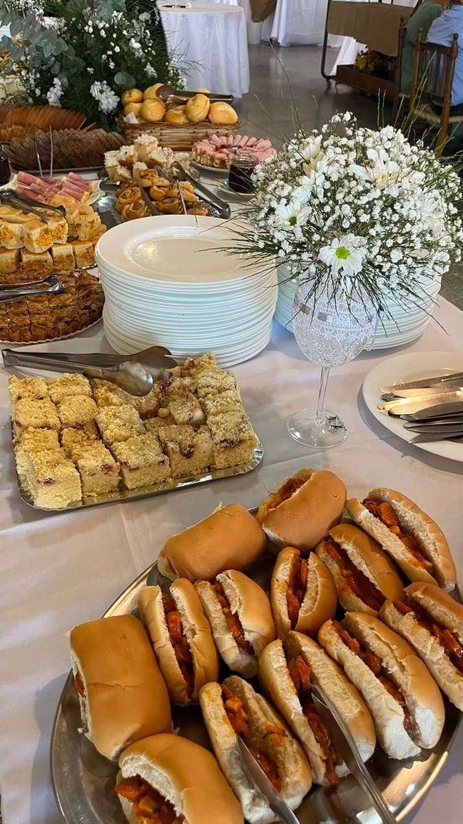 Mesa de festa com mini cachorros-quentes, bolos e salgados