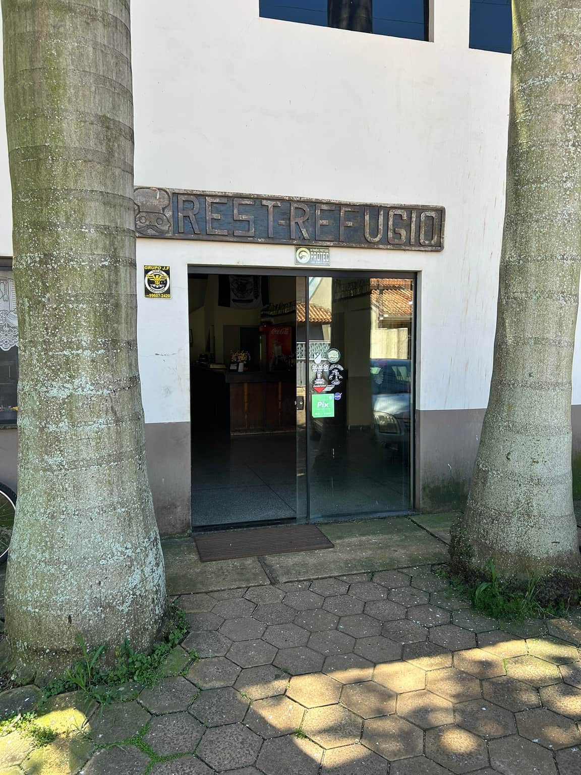 Entrada do Restaurante Refúgio, com a placa de madeira entre duas palmeiras