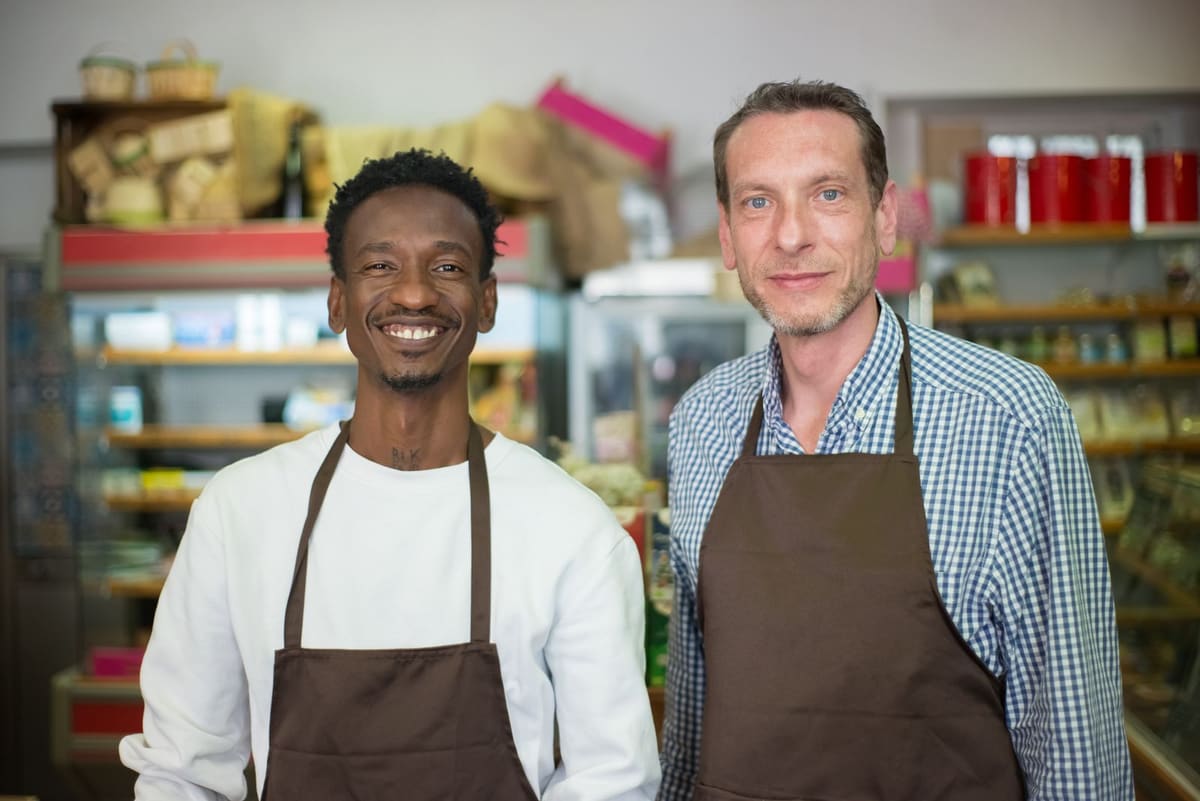 Dois donos de uma mercearia sorrindo, de avental